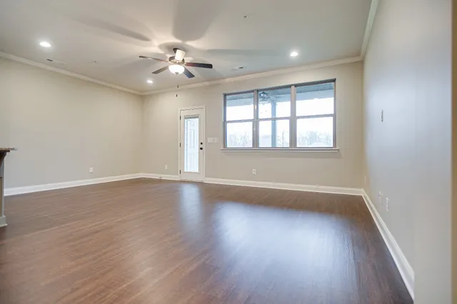 an empty room with wooden floor fan and windows