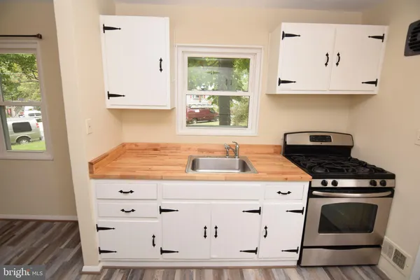 a kitchen with granite countertop a stove a sink and white cabinets with wooden floor