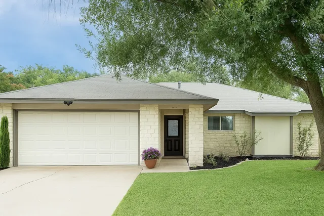 a view of a house with a yard plants and large tree