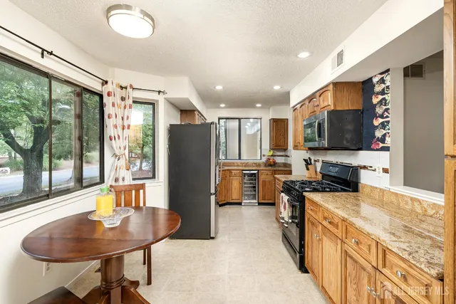 a kitchen with stainless steel appliances granite countertop a refrigerator a sink a stove and a dining table with wooden floor