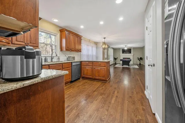 a kitchen with stainless steel appliances granite countertop a stove top oven a sink a refrigerator and white cabinets with wooden floor