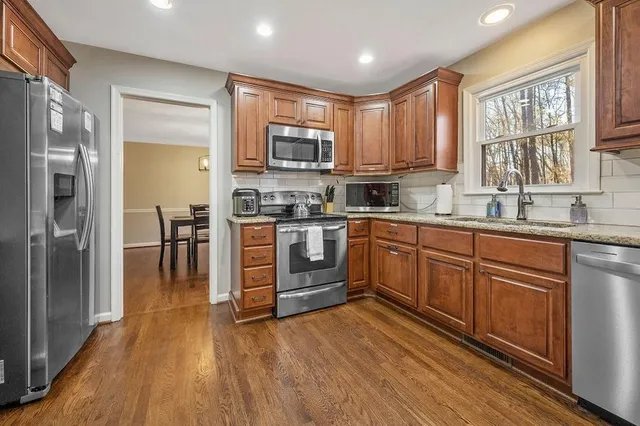 a kitchen with a sink wooden floor stainless steel appliances and windows