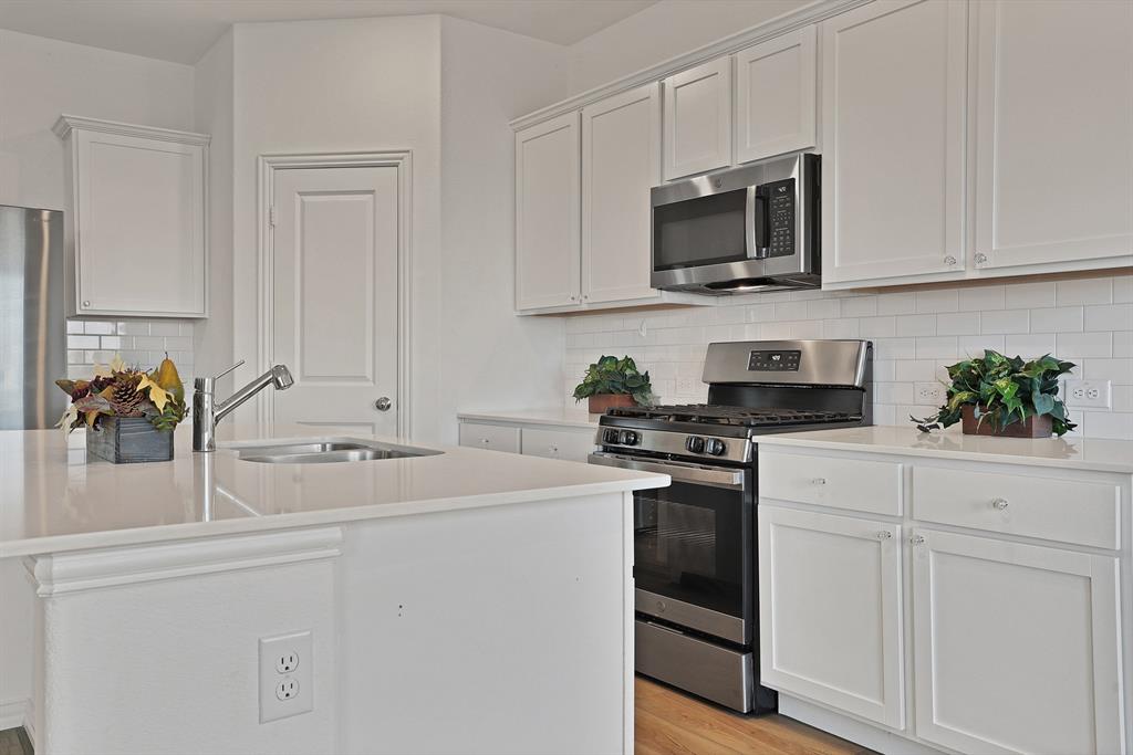 3204 Renaissance Drive Denton, TX 76207 - Photo 10 of 25 Modern kitchen featuring white shaker cabinetry, stainless steel appliances, a subway tile backsplash, light-toned countertops, and a kitchen island with an integrated sink