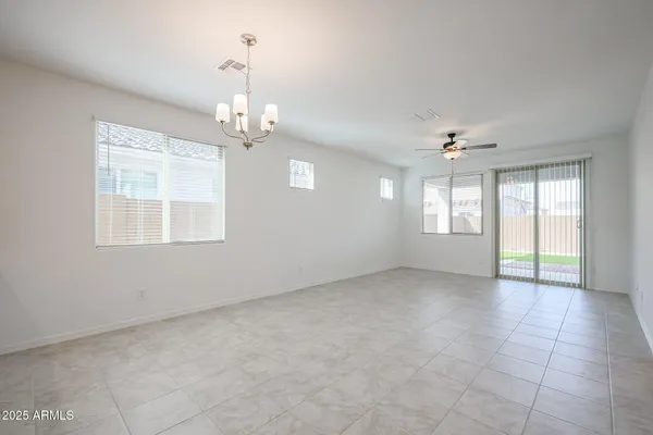 an empty room with chandelier fan and windows