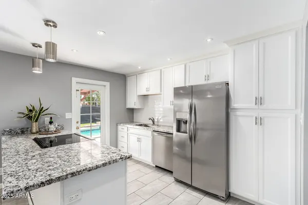 a kitchen with stainless steel appliances granite countertop a refrigerator a sink a stove and white cabinets