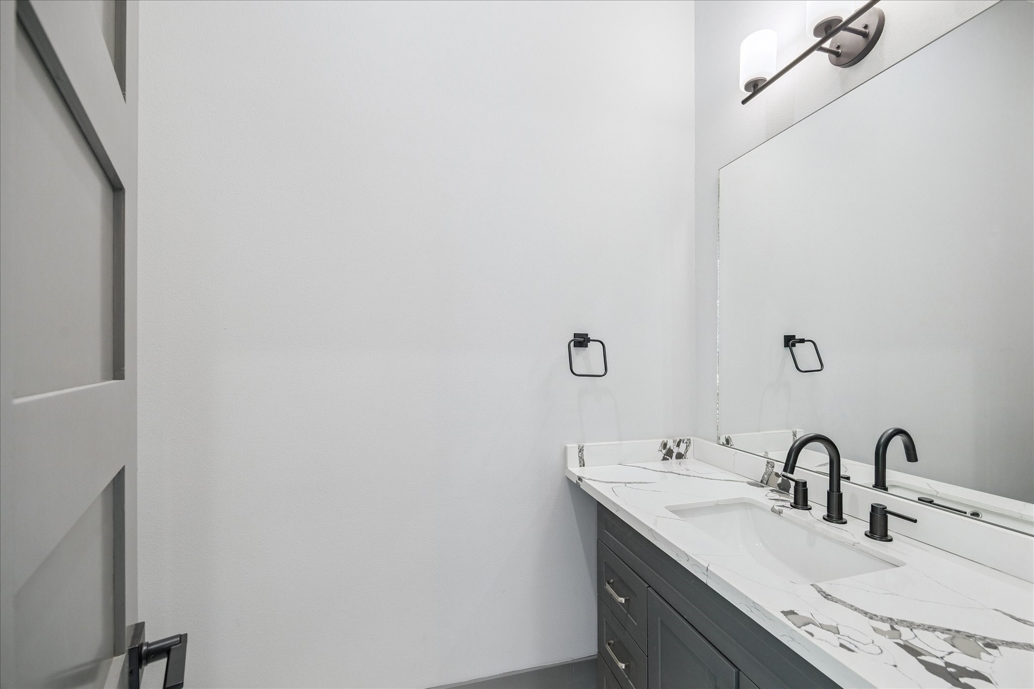 2319 Tuam Street Houston, TX 77004 - Photo 13 of 28 Quartz counters with striking veining and matte black fixtures bring a modern touch to the powder bath. A spacious mirror and wall-mounted lighting ensure a bright, inviting atmosphere that balances practicality with style.