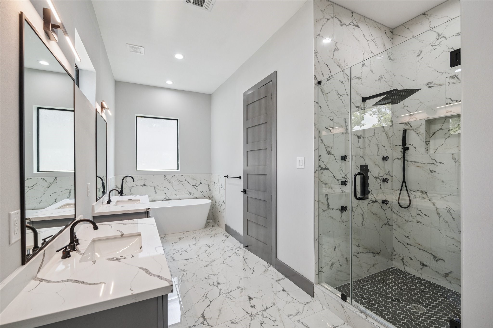 2319 Tuam Street Houston, TX 77004 - Photo 17 of 28 The primary bathroom is anchored by dual vanities, a glass-enclosed shower, and a soaking tub set beneath a window. Coordinated tilework ties the space together, accented by dark fixtures for contrast.
