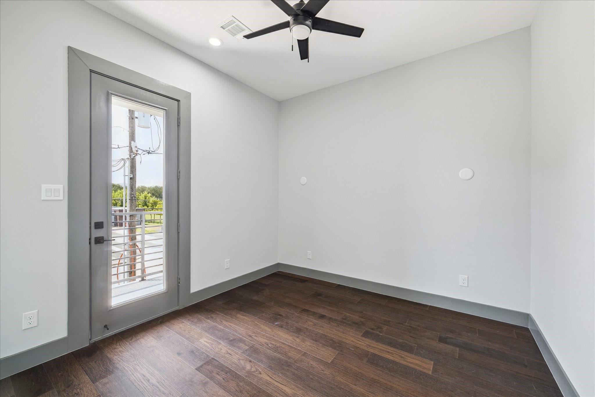 2319 Tuam Street Houston, TX 77004 - Photo 24 of 28 This secondary bedroom features warm hardwood flooring, neutral walls, and a ceiling fan for year-round comfort. A glass door leads directly onto a private balcony, creating an inviting space that blends indoor and outdoor living.