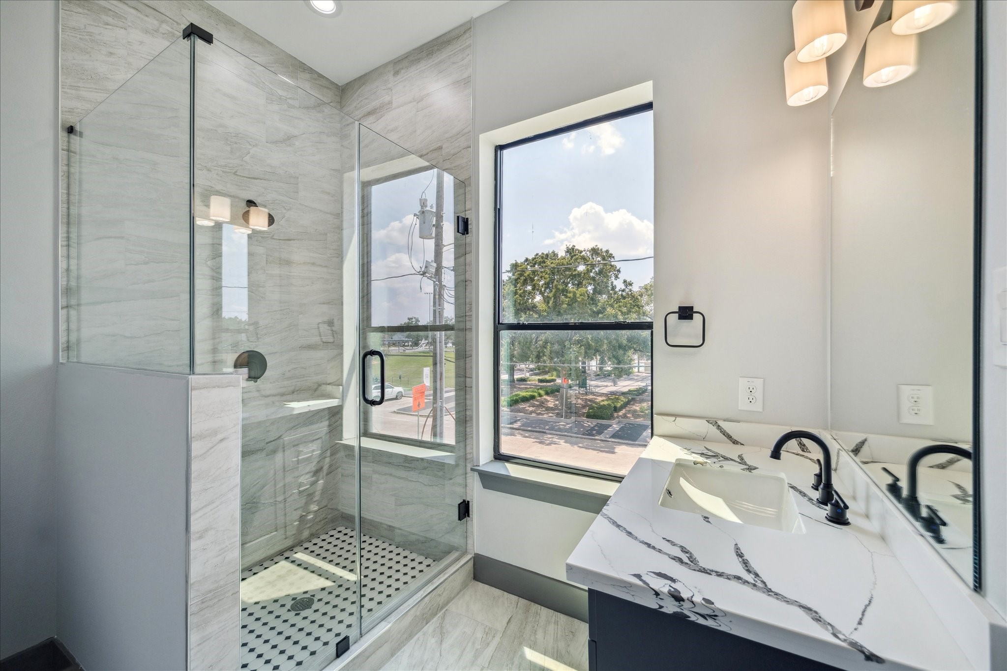 2319 Tuam Street Houston, TX 77004 - Photo 25 of 28 Bright and inviting, this bathroom showcases a walk-in shower with frameless glass and tile surround, paired with a vanity topped in quartz with clean-lined fixtures. A large window allows natural light to fill the space while offering a view toward the front of the property.