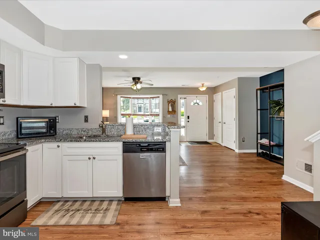 a kitchen with granite countertop a stove top oven a sink dishwasher and white cabinets with wooden floor