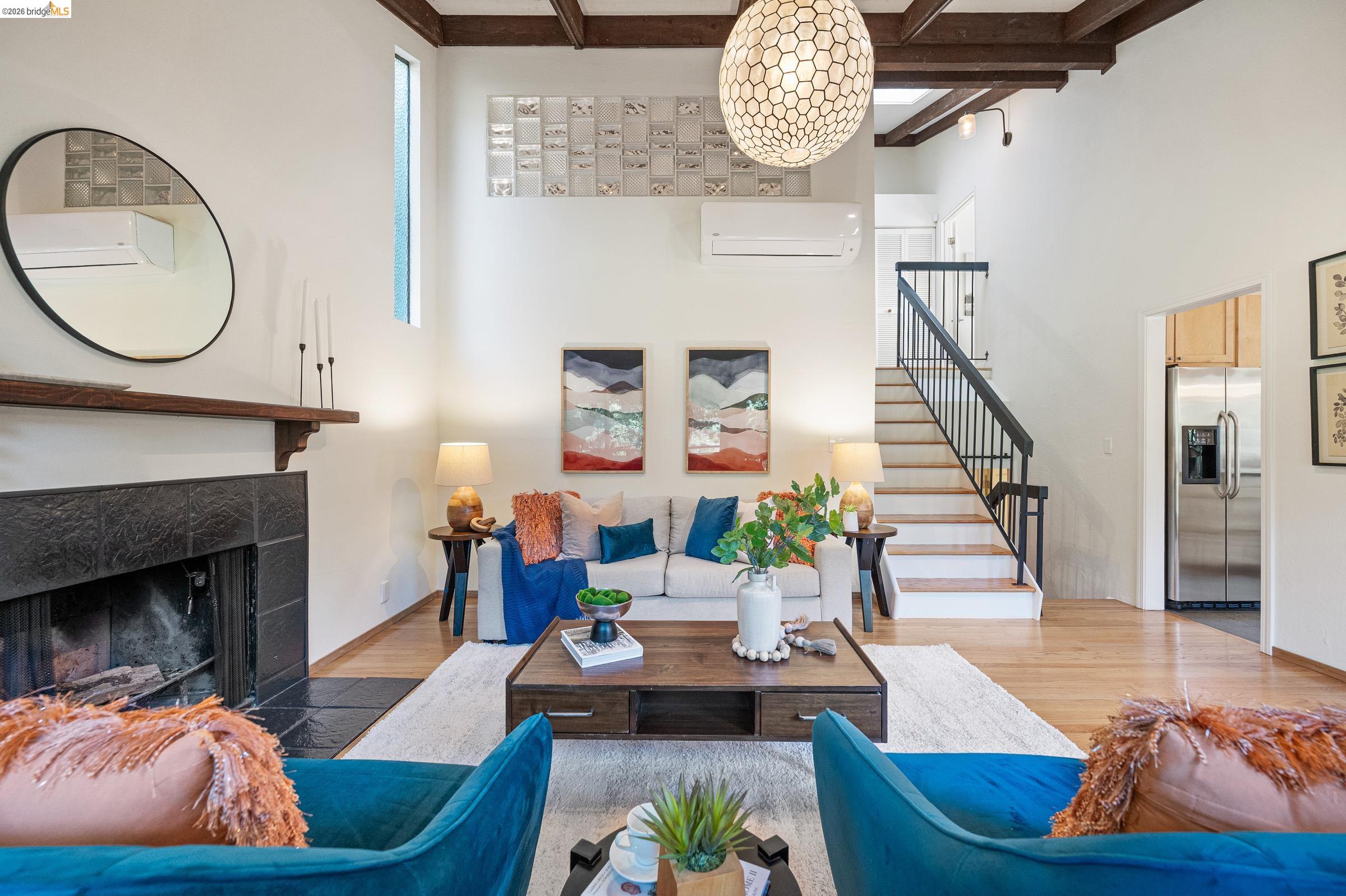 6600 Heather Ridge Way Oakland, CA 94611 - Photo 9 of 66 Living area featuring a high ceiling with exposed wood beams, a sleek fireplace with dark tile surround and wood mantle, wood-finish flooring, a contemporary spherical pendant light, and a staircase with dark metal railings