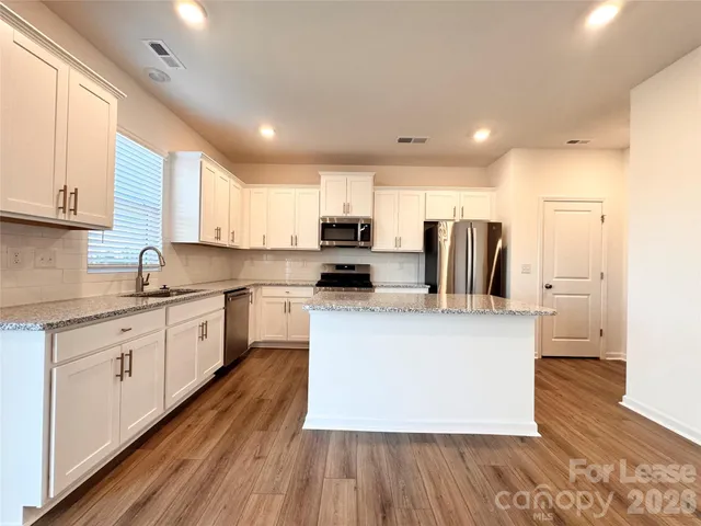 a kitchen with a refrigerator a sink dishwasher a stove and white cabinets with wooden floor