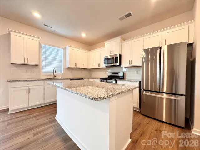 a kitchen with kitchen island granite countertop white cabinets and stainless steel appliances