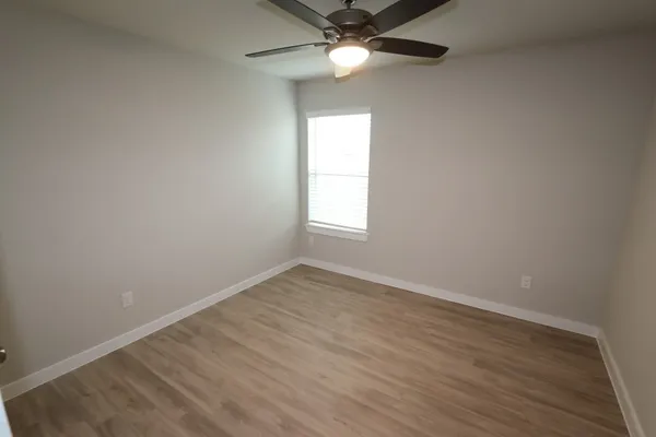 an empty room with wooden floor fan and windows