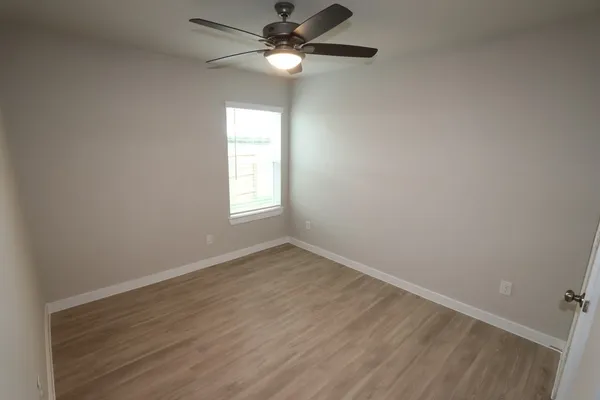 an empty room with wooden floor fan and windows