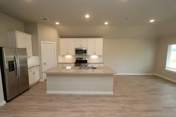 a view of a kitchen with stainless steel appliances granite countertop a stove a refrigerator a sink a microwave and wooden floor