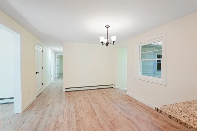 an empty room with wooden floor chandelier and windows