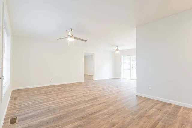 a view of an empty room with wooden floor and a ceiling fan