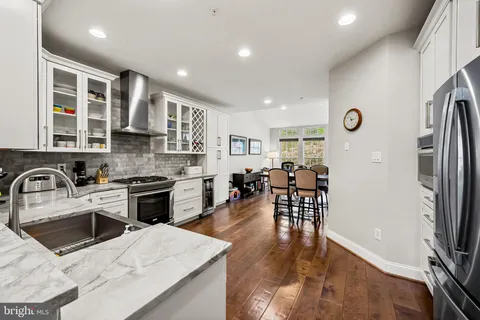 a kitchen with stainless steel appliances granite countertop a refrigerator a stove top oven a sink dishwasher and white cabinets with wooden floor