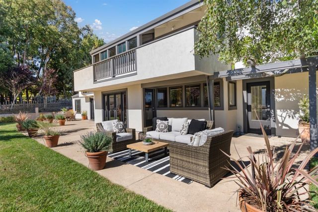 a view of a patio with couches table and chairs and potted plants and large trees