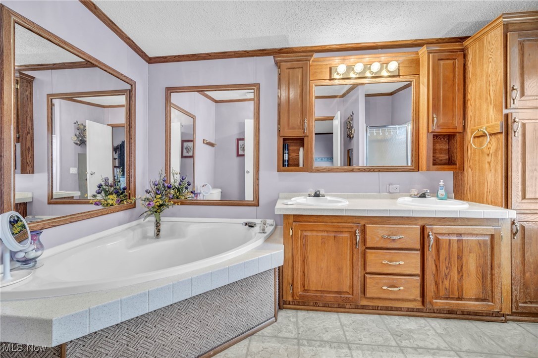 27202 Cook Road, Unit 95 Olmsted Falls, OH 44138 - Photo 23 of 46 Bathroom featuring a textured ceiling, double vanity, a garden tub, and crown molding