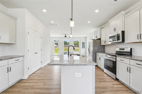 a kitchen with stainless steel appliances granite countertop a stove top oven a sink a refrigerator and white cabinets with wooden floor