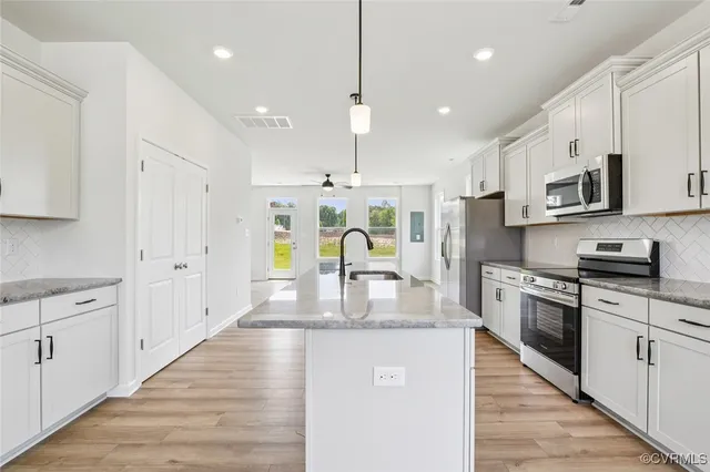 a kitchen with stainless steel appliances granite countertop a stove top oven a sink a refrigerator and white cabinets with wooden floor