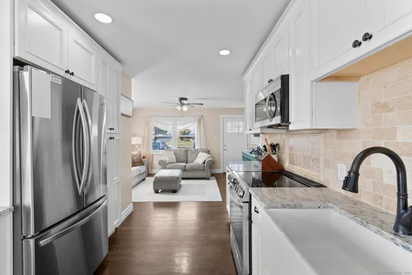 a kitchen with refrigerator a sink a stove and white cabinets with wooden floor