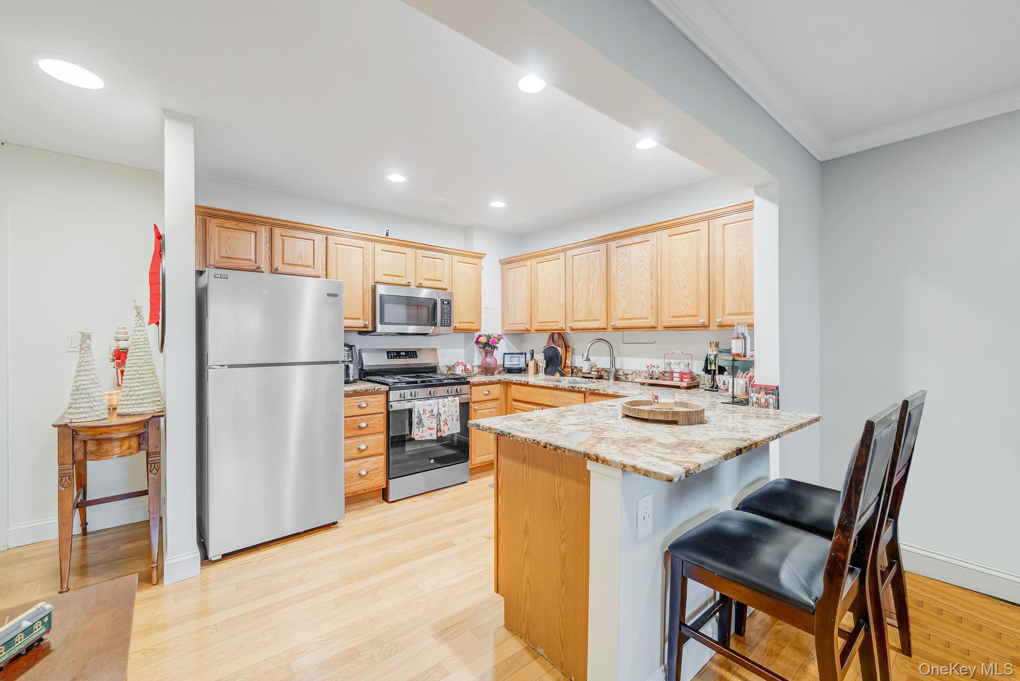 124 Smith Street, Unit 3F Freeport, NY 11520 - Photo 6 of 15 Kitchen with light brown cabinets, stainless steel appliances, a breakfast bar, light wood finished floors, and a peninsula