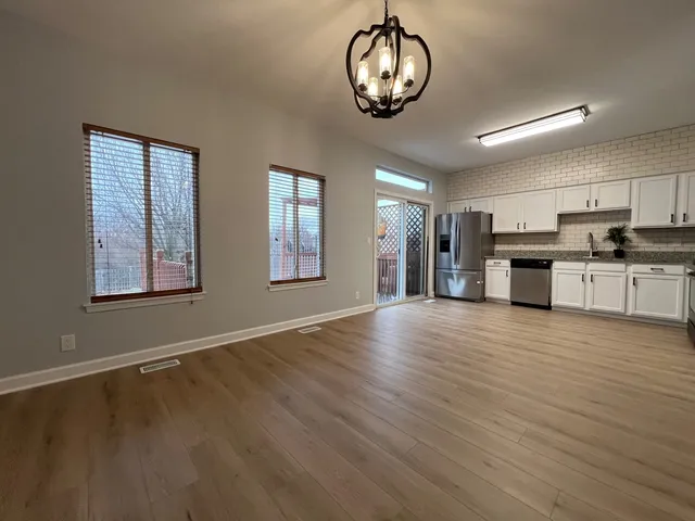 an empty room with wooden floor and kitchen view