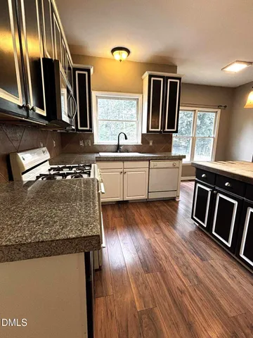 a kitchen with stainless steel appliances granite countertop a stove a sink dishwasher a microwave oven and a dining table with wooden floor