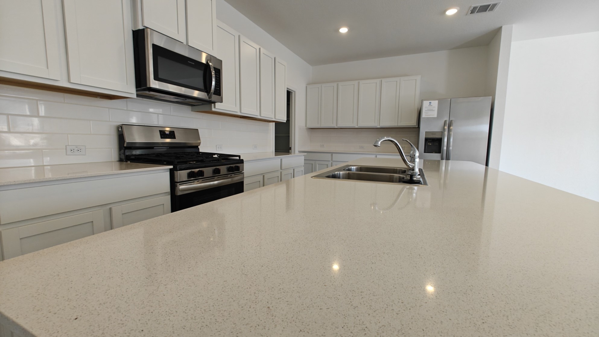 Kitchen with stainless steel appliances, light stone counters, white cabinetry, recessed lighting, and tasteful backsplash