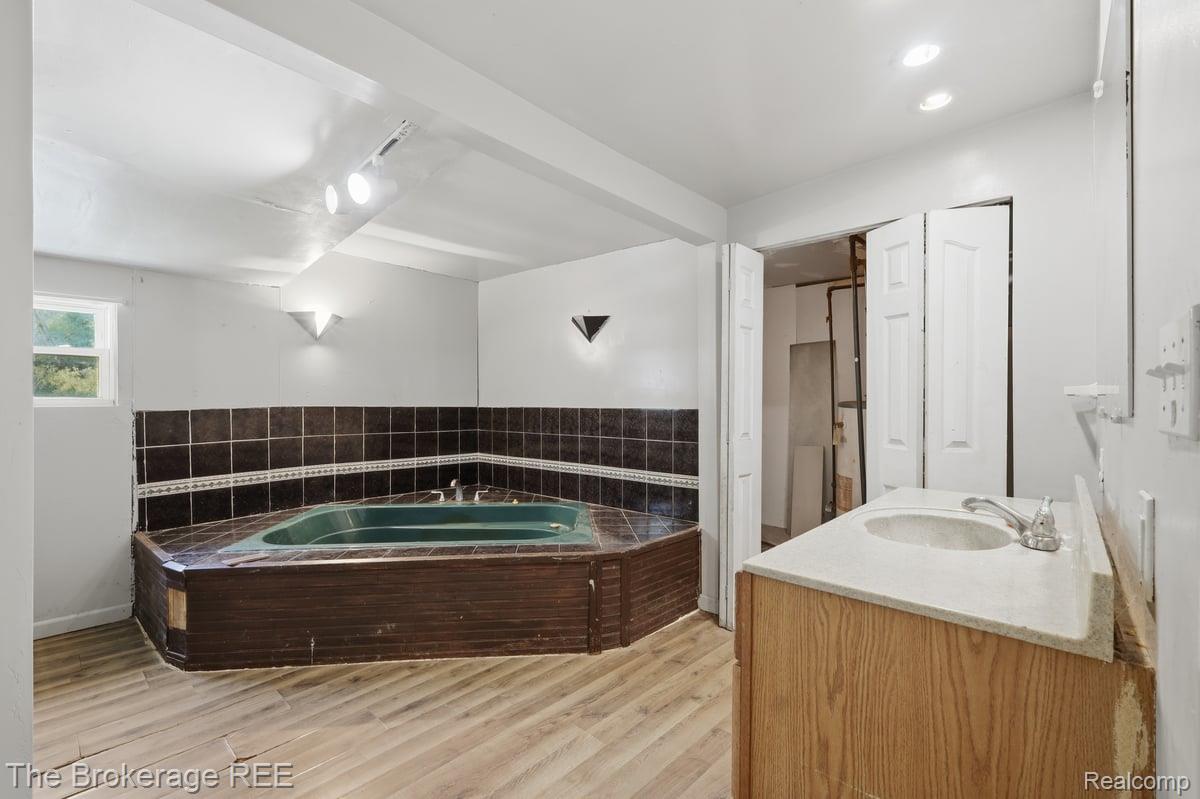 10135 Clark Road Davison, MI 48423 - Photo 30 of 38 Enclosed corner soaking tub with dark tile surround, light wood-finish flooring, and single window