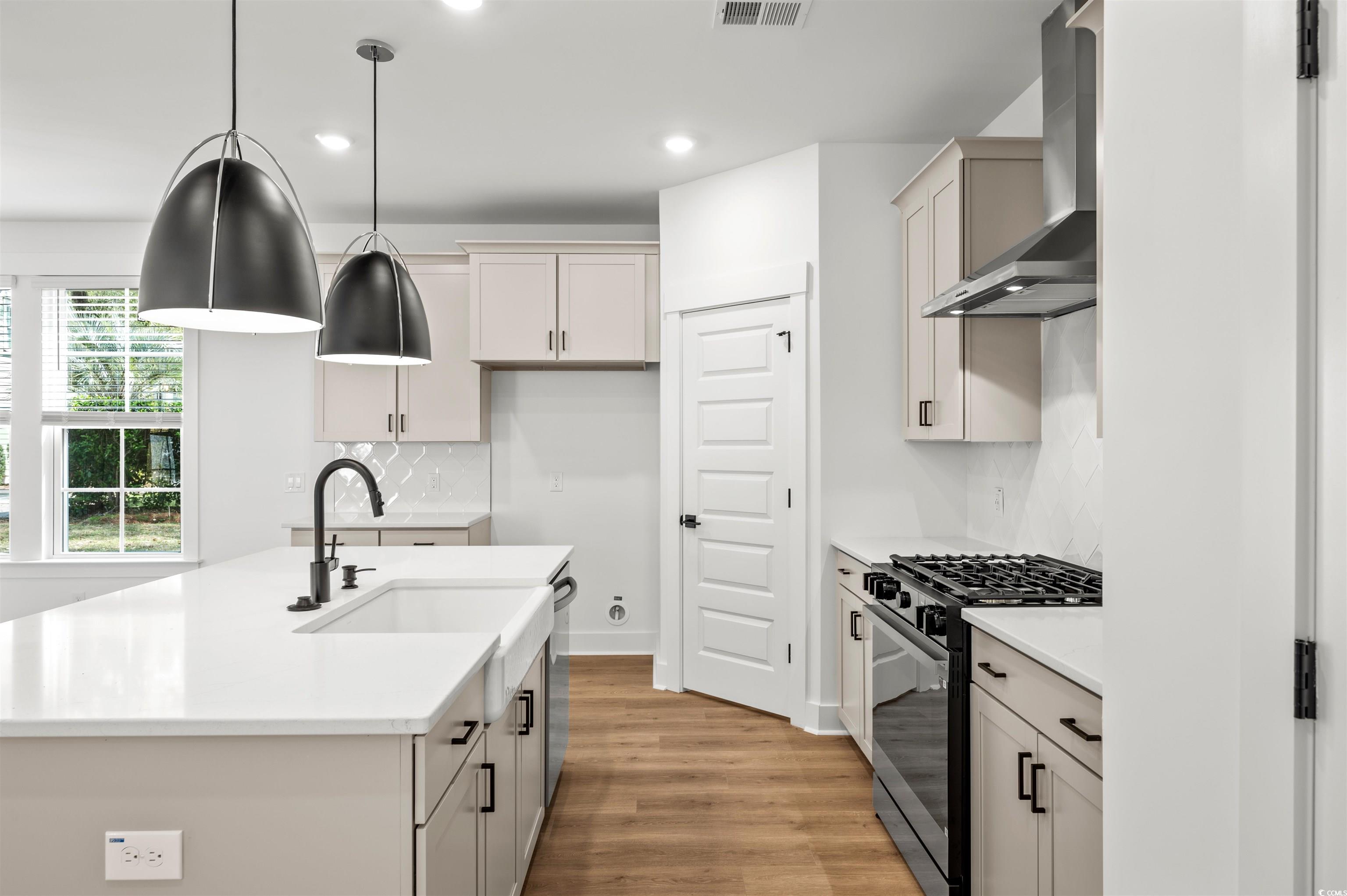 67 Bridge View Road Georgetown, SC 29440 - Photo 6 of 40 Kitchen with decorative backsplash, black gas range, wall chimney range hood, light stone countertops, and decorative light fixtures