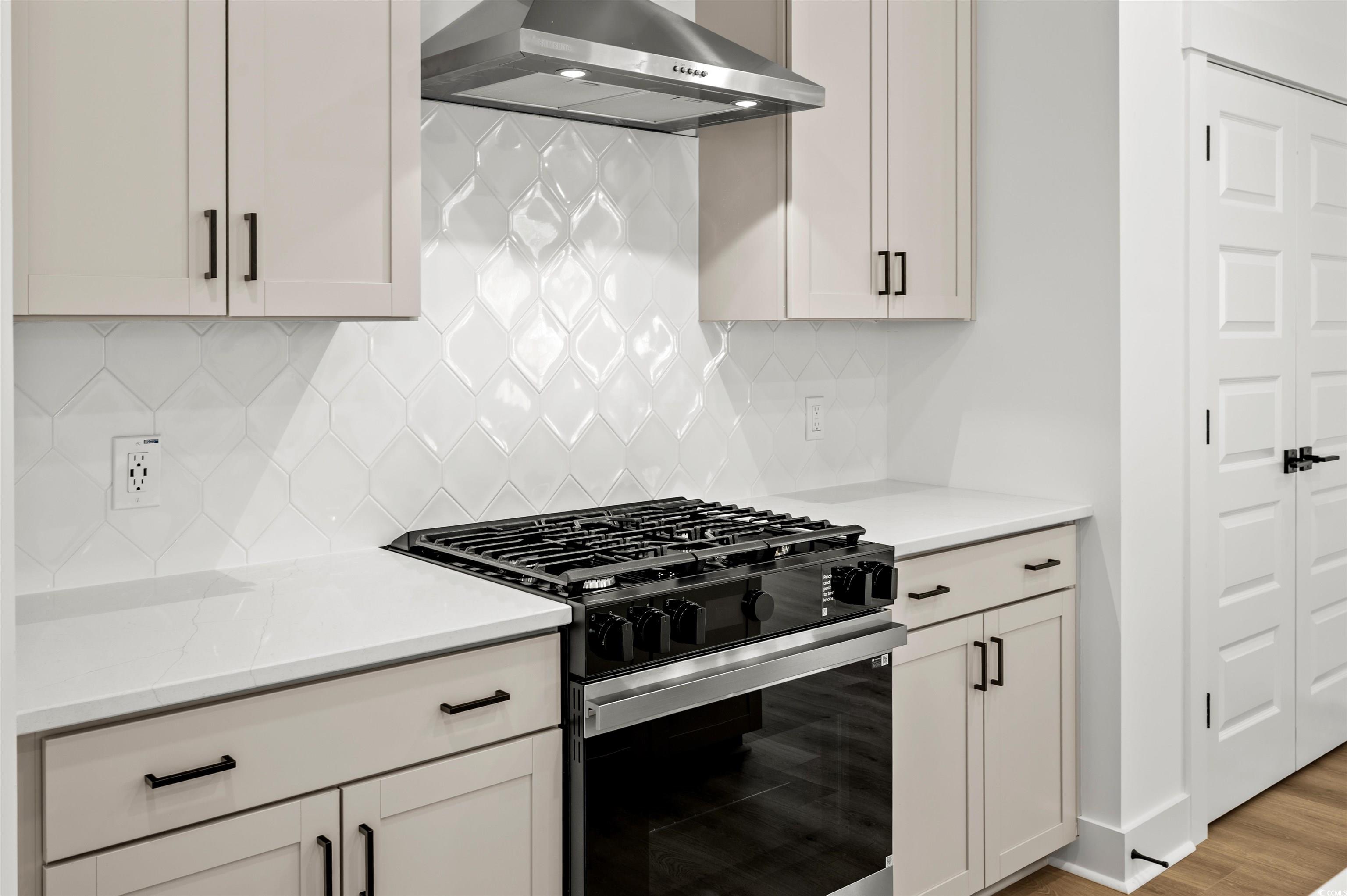 67 Bridge View Road Georgetown, SC 29440 - Photo 8 of 40 Kitchen featuring gas range, wall chimney exhaust hood, white cabinets, tasteful backsplash, and light stone countertops