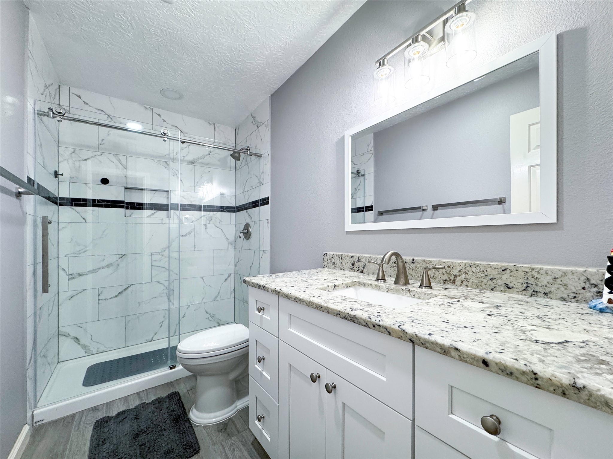 6618 Wimbledon Trail Road Spring, TX 77379 - Photo 34 of 44 Nestled within the upstairs en-suite, designed with a spa-inspired aesthetic, this beautifully updated bathroom features sleek granite countertops, custom cabinetry, and designer lighting that elevates everyday living. The glass-enclosed shower showcases elegant marble-style tile with a refined accent band, creating a clean, timeless look. Thoughtful finishes and a serene color palette complete this luxurious retreat.