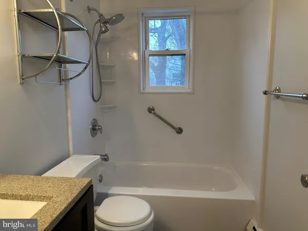 a bathroom with a granite countertop bathtub shower sink vanity and toilet