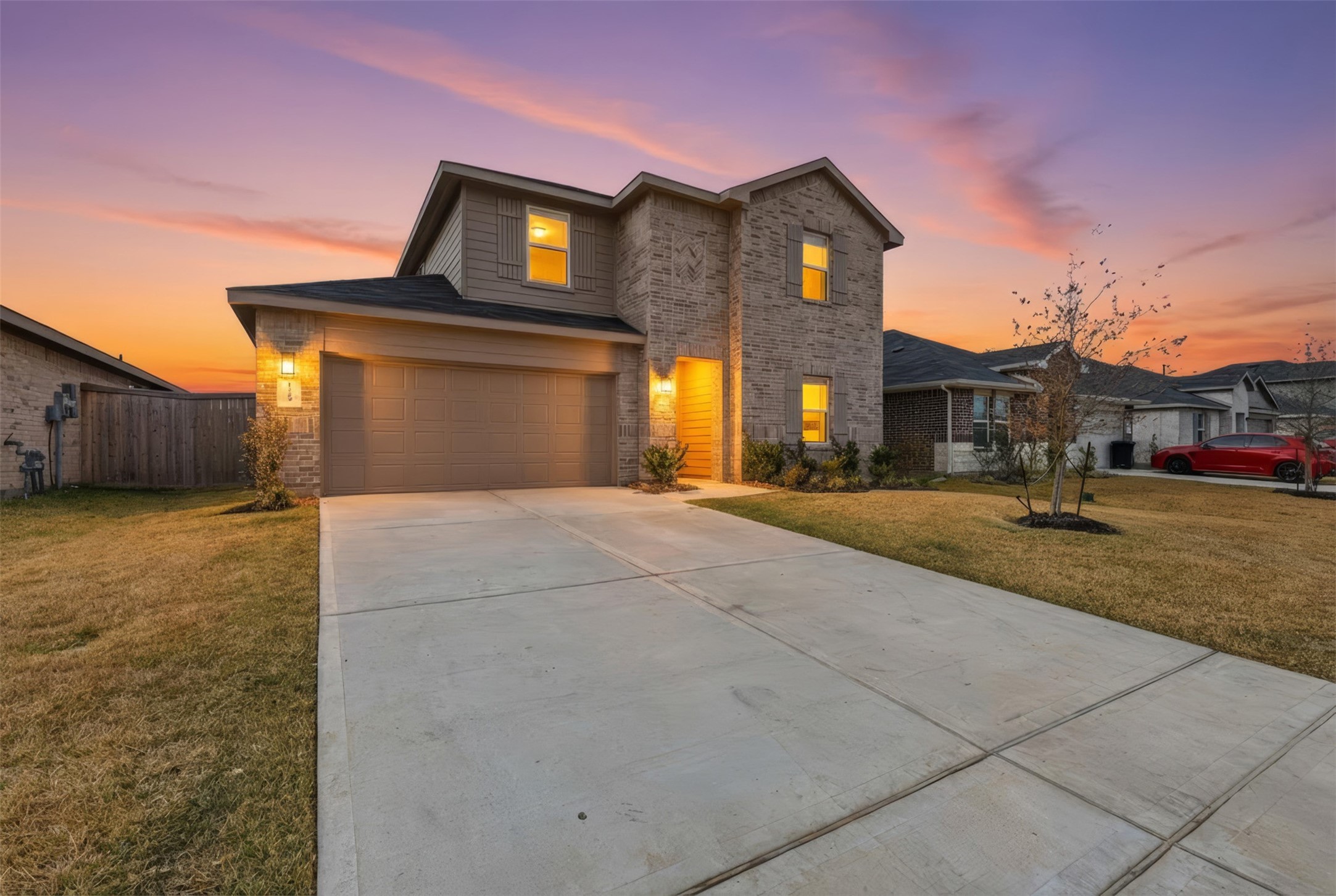 This is a modern two-story home with a brick facade and a spacious driveway leading to a two-car garage. The exterior is well-lit and features a neatly maintained lawn.