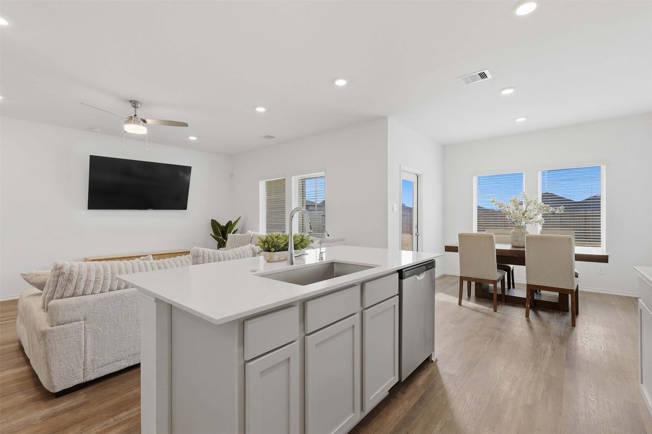 17719 Winfall Drive Crosby, TX 77532 - Photo 13 of 47 This photo showcases a bright, open-concept living area with a modern kitchen island, cozy seating, and a dining space. The room features recessed lighting, a ceiling fan, and large windows for natural light, creating an inviting and spacious atmosphere.