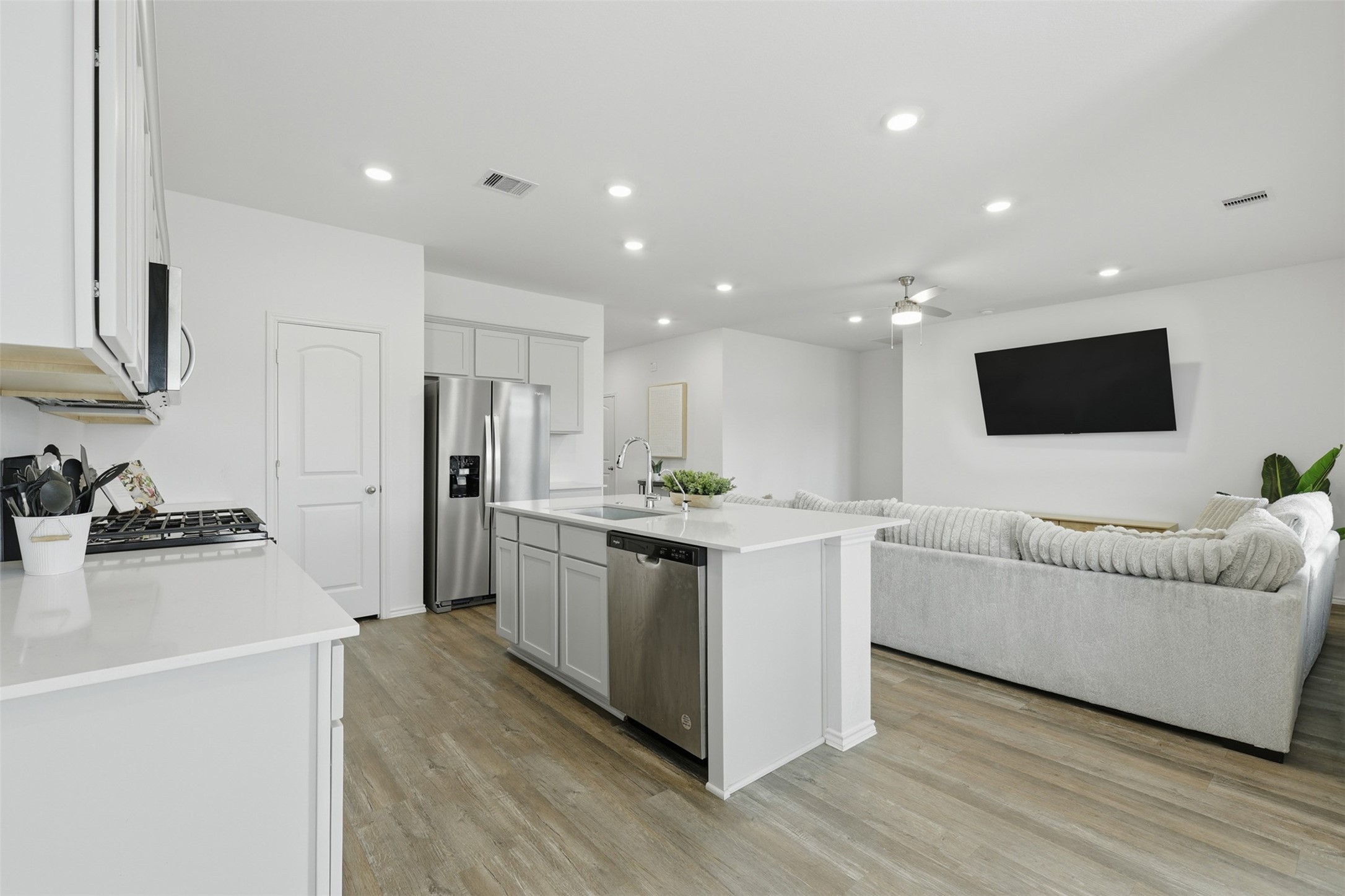 17719 Winfall Drive Crosby, TX 77532 - Photo 14 of 47 This photo shows a modern, open-concept kitchen and living area with sleek white cabinetry, stainless steel appliances, and a large island.