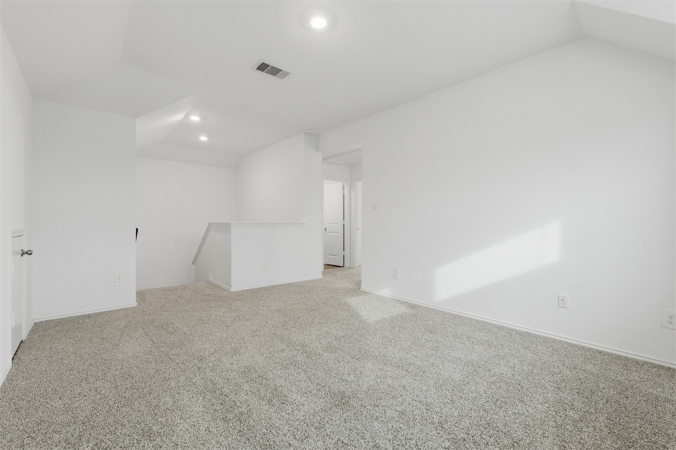 17719 Winfall Drive Crosby, TX 77532 - Photo 28 of 47 This photo shows a bright, spacious upstairs game room area with neutral carpeting and white walls. The layout includes recessed lighting and a railing overlooking the stairs, leading to a hallway with a door.