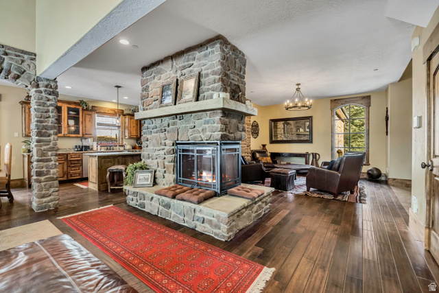 9049 Timphaven Road Sundance, UT 84604 - Photo 6 of 63 Living area with dark wood-style floors, a chandelier, a fireplace, decorative columns, and a textured ceiling