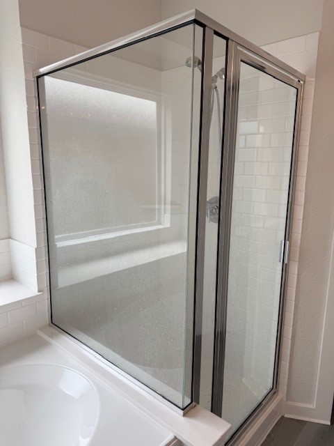 7838 Ruth Ravine Court Spring, TX 77379 - Photo 11 of 23 This photo shows a modern bathroom with a glass-enclosed corner shower and partial view of a bathtub, featuring white tile walls and a sleek design.