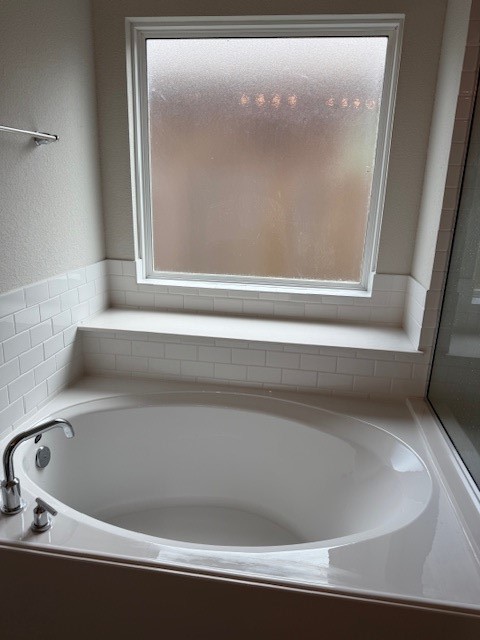 7838 Ruth Ravine Court Spring, TX 77379 - Photo 12 of 23 This bathroom features a spacious white bathtub with modern fixtures, set against a wall with white subway tiles. A large frosted window provides natural light while ensuring privacy.
