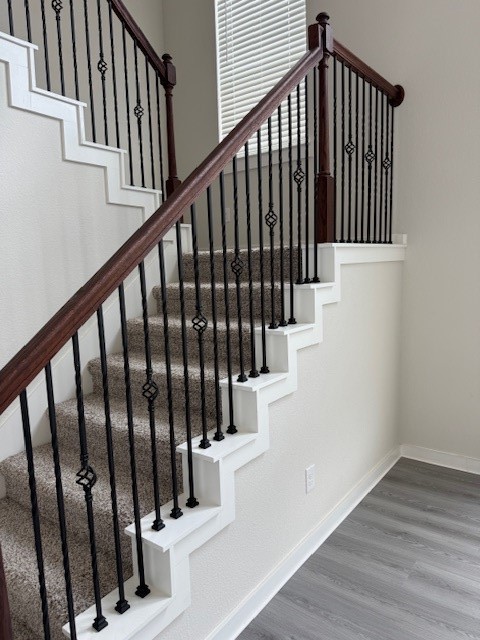 7838 Ruth Ravine Court Spring, TX 77379 - Photo 14 of 23 A modern staircase features carpeted steps, dark metal railings with decorative elements, and a wooden handrail. The space is brightened by natural light from a nearby window, and the surrounding area has light-colored walls and sleek flooring.
