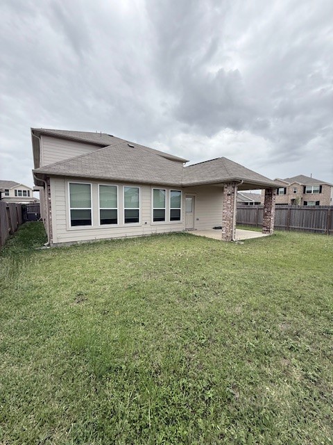 7838 Ruth Ravine Court Spring, TX 77379 - Photo 23 of 23 This photo shows the backyard of a house featuring a spacious lawn, a two-story structure with light-colored siding, and multiple windows. There's a covered patio area supported by brick columns, and the yard is enclosed by a wooden fence.