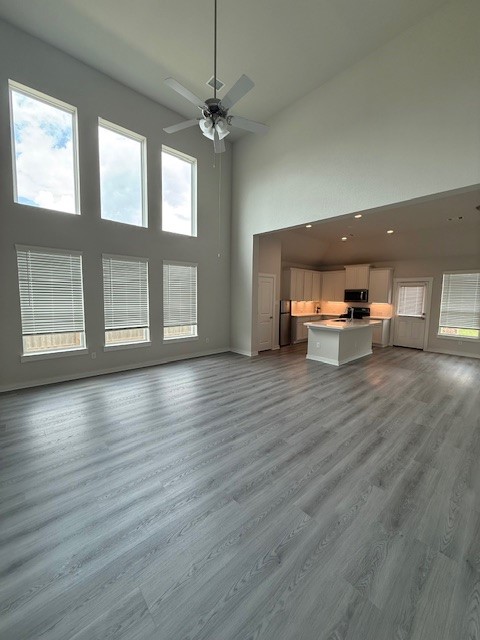 7838 Ruth Ravine Court Spring, TX 77379 - Photo 4 of 23 This photo showcases a spacious, open-concept living area with high ceilings and abundant natural light from large windows. The room features modern grey flooring and includes a view of a bright kitchen with white cabinetry and an island.