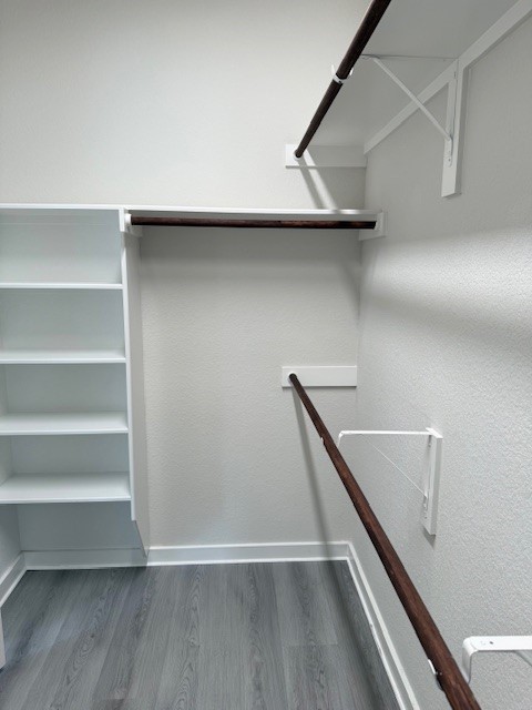 7838 Ruth Ravine Court Spring, TX 77379 - Photo 9 of 23 This photo shows a spacious walk-in closet with sleek, dark wood rods for hanging clothes and white built-in shelving. The flooring is a modern gray laminate, and the walls are painted a light neutral color, creating a clean and organized space.