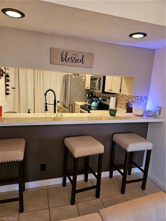 4120 Looking Glass Lane, Unit 3708 Naples, FL 34112 - Photo 11 of 25 Kitchen featuring a breakfast bar, light countertops, appliances with stainless steel finishes, tasteful backsplash, and light tile patterned floors