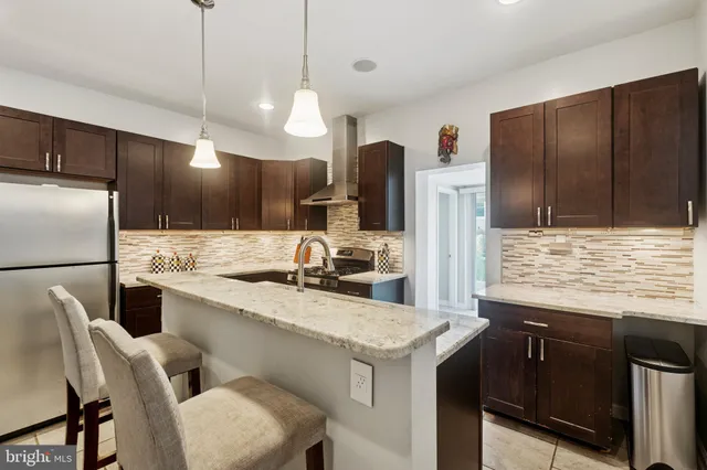 a kitchen with stainless steel appliances granite countertop a sink a stove a refrigerator and island with wooden cabinets